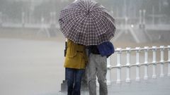 Dos personas comparten paraguas bajo la lluvia este viernes, en la Playa de San Lorenzo, Gijón