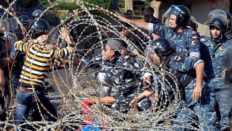 Varios manifestantes se enfrentan a los agentes de policía mientras tratan de traspasar la concertina que los separa para dirigirse hacia el Parlamento