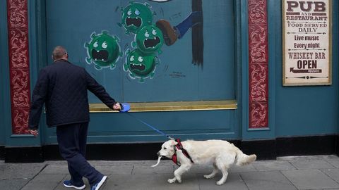 Un hombre pasea a su perro por una calle de Dublín en la que hay pintado un mural sobre el covid-19