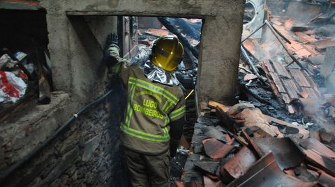 Un bombero examina el interior de la casa que se incendió este jueves en la parroquia de Doade (Sober)