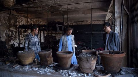 Un polica afgano y residentes locales inspeccionan una tienda quemada por el ataque de un coche bomba, en Kabul