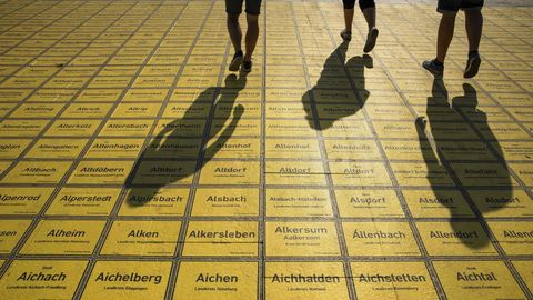 Gente caminando entre aceras con nombres de lugares de ciudades alemanas escritos cerca de la estacin de trenes en Berln 
