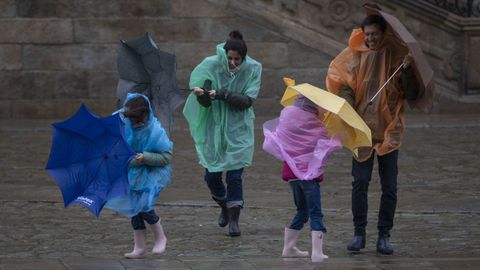 Una familia trata de protegerse de la lluvia en medio del fuerte viento, este martes en la Praza do Obradoiro