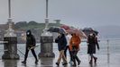 Un grupo de personas paseando por la playa de San Lorenzo ante un tiempo de frío y lluvia