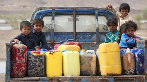 Varios nios viajan en la parte de atras de un vehculo junto a bidones de agua en un campament en Marib (Yemen).