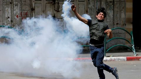 Un manifestante palestino devuelve un bote de gas lacrimgeno disparado por las tropas israeles durante los enfrentamientos en Hebrn, en Cisjordania