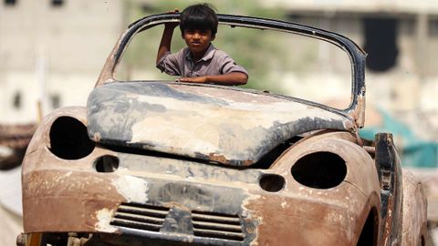 Un niño observa al fotógrafo desde un coche desguazado a las afueras de Karachi, Pakistán