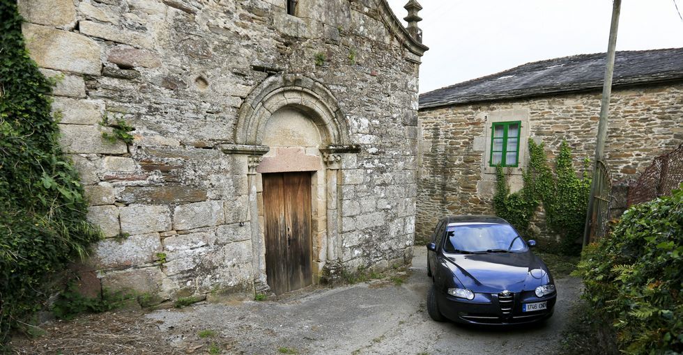Un coche peque�o pasa a duras penas por la curva que est� entre una casa y la iglesia. 