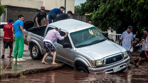 Gente intentando mover un coche para evitar que sea arrastrado por el agua en una calle inundada en Culiacn, Mxico