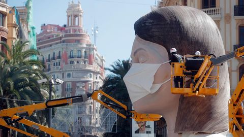 Unos operarios colocan una mascarilla a la figura principal de la plaza del ayuntamiento de Valencia, suspendidas las fallas