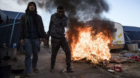 Dos inmigrantes caminan junto a una estructura en llamas durante el proceso de desmantelamiento de la Jungla de Calais