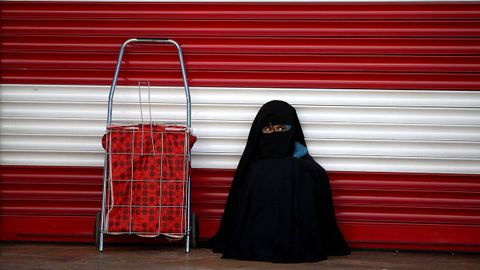 Una mujer cubierta con un chador descansa junto a una tienda cerrada en Sanliurfa (Turqua) 