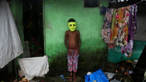 Un nio se refugia de la lluvia fuera de su casa en India
