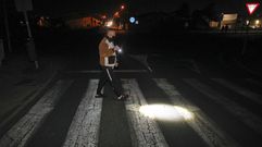 Un vecino iluminando con una linterna el paso de peatones para cruzar la carretera.
