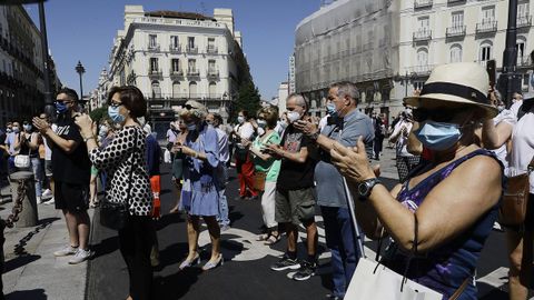 Transentes aplauden al finalizar el minuto de silencio en memoria por los fallecidos por el covid-19 en la sede de la Comunidad de Madrid