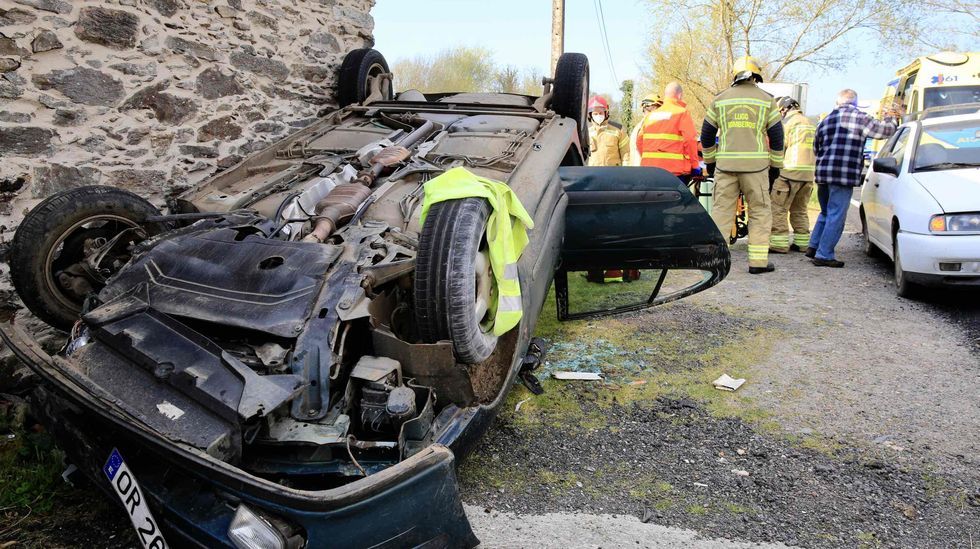 Sanitarios y bomberos trasladan a la ambulancia en camilla a uno de los ocupantes del coche que volc&oacute;