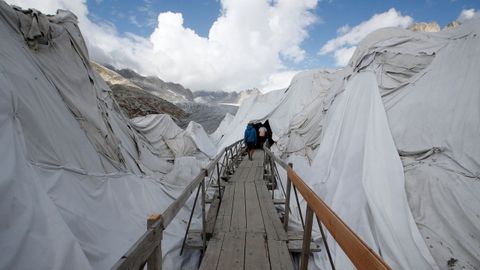 Varias personas entran en la llamada Cueva de Hielo, cubierta para evitar que el hielo se derrita, en el glaciar Rhone en Furka (Suiza)