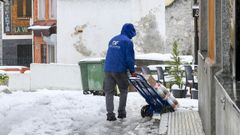 Un repartidor camina por una calle cubierta de nieve en la localidad asturiana de Aller