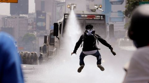 Un manifestante salta para evitar un chorro de agua lanzado desde un vehículo antidisturbios en una manifestación contra Nicolás Maduro en Caracas (Venezuela).