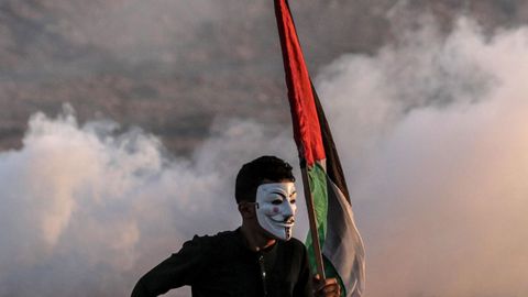 Un palestino con una mscara de Guy Fawkes ondea la bandera nacional durante los disturbios cerca de la frontera martima entre Israel y Gaza