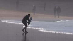 Un hombre con un beb en brazos frente a las olas de la playa de San Lorenzo