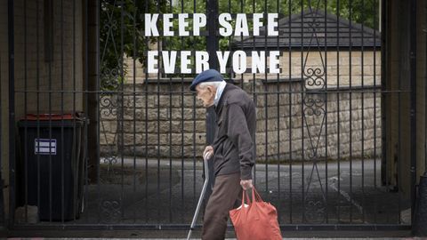 Un anciano pasa por delante de la puerta de un parque escocs cerrado en el que se puede leer mantnganse todos a salvo