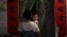Una niño observa a la cámara mientras su madre lo lleva en brazos en la entrada de una casa en Sanya (China)