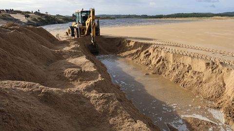 Trabajos de apertura del canal con una excavadora en la playa de Valdovio.