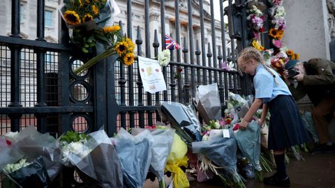 Una niña deposita flores en el palacio de Buckingham