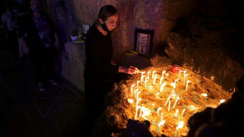 Una mujer, con la mascarilla apartada, enciende velas en una iglesia de Nazaret
