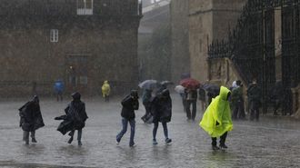 Turistas y peregrinos cruzan la plaza del Obradoiro bajo una intensa lluvia.