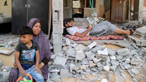 Un hombre palestino descansa entre las ruinas de una vivienda mientras una mujer sostiene a un niño en el regazo, en la Franja de Gaza
