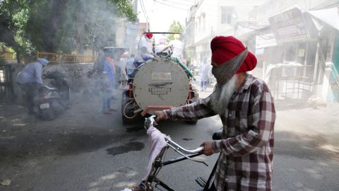 Un trabajador rocía desinfectante en una calle de la localidad india de Amritsar, ante la mirada de los transeúntes