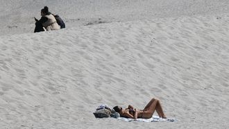 Esta imagen, del jueves 18 de abril, refleja las dos Coruñas enfrentadas en cuestión de playa: una mujer toma el sol mientras otra va protegida del frío con un plumífero