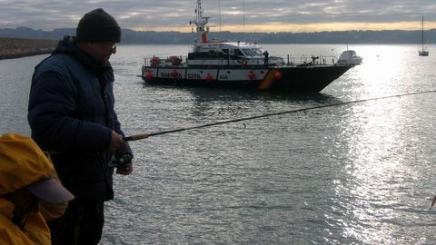 Pescadores recreativos practicando su afición en la costa gallega, con una patrullera de la Guardia Civil al fondo, en una imagen de archivo.