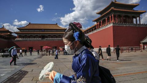 Una mujer vestida con el traje tradicional camina ante la Ciudad Prohibida de Pekín