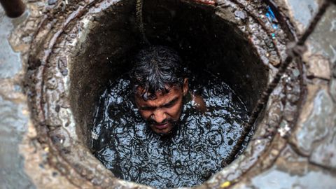 Joney, un empleado de la limpieza de la red de alcantarillado, asoma la cabeza por una alcantarilla mientras trabaja sin ningún equipo de seguridad, en Ghaziabad (India)