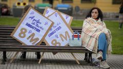Una mujer con sus pancartas sentada en un banco antes de participar en la marcha que conmemora el Día de la Mujer