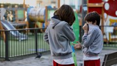 Dos nios se tapan la boca con sudaderas ante un parque cerrado en la Plaza de Galicia de Santiago