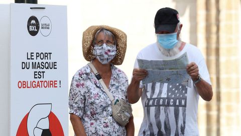 Personas usando mascarillas junto a un aviso que indica la obligatoriedad de las mismas en Bruselas, Blgica.