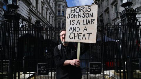A protester protests outside Downing Street with a sign accusing Boris Johnson of lying and cheating.