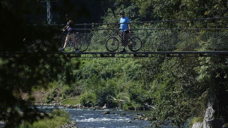 Unos ciclistas pasan por una pasarela sobre el río Nalónen en Las Caldas (Asturias)