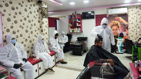 En Calcuta, un peluquero corta el pelo a un cliente mientras otros aguardan vestidos con trajes de proteccin