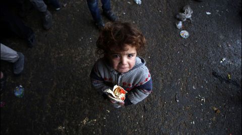 Un nio sirio, que huy con su familia de las zonas controladas por los rebeldes en la ciudad de Alepo, llora mientras sostiene un bocadillo en un refugio en Jibrin, al este de Alepo (Siria)