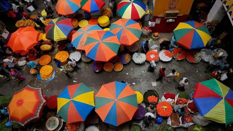 Varios vendedores se sientan debajo de las sombrillas para tratar de escapar del calor en un mercado de flores en India. 