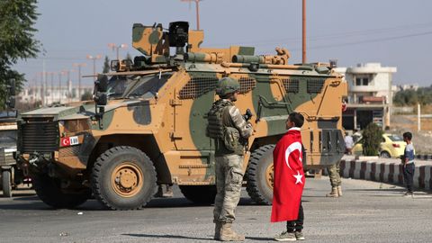 Un nios vestido con la bandera turca saluda a uno de los soldados despelgados en Tal Abiad