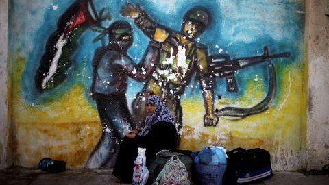 Una mujer sentada delante de un mural esperando un permiso que la permita pasar a Egipto a travs de Rafah (Palestina).