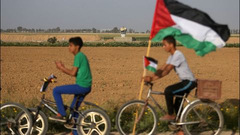Dos nios palestinos llevan la bandera de su pas frente a la frontera con Israel