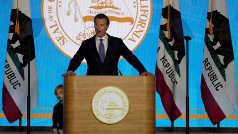 El gobernador de California, Gavin Newsom (c), habla mientras su hijo Dutch (i), de dos aos, se asoma por detrs del podio