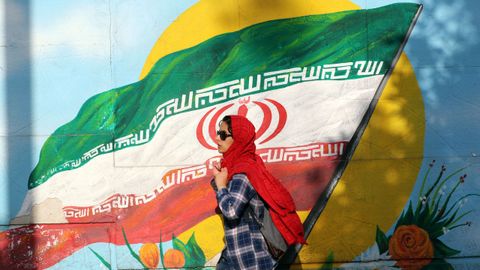 Una mujer iraní pasa frente a un mural con la bandera del país.